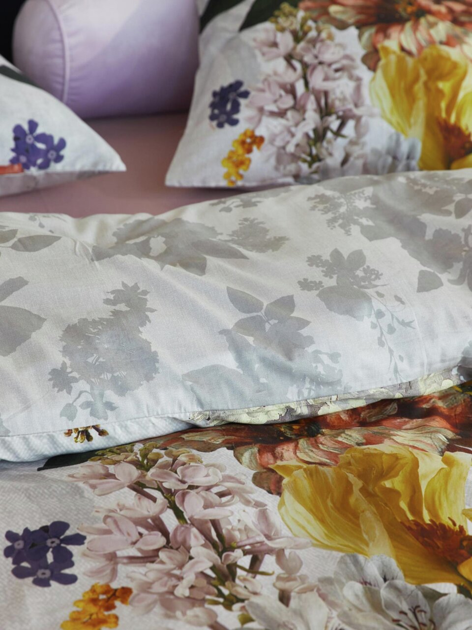 Nahaufnahme von Bettwäsche mit floralem Muster in verschiedenen Farben, darunter Gelb, Lila und Rosa, auf einem Bett.
