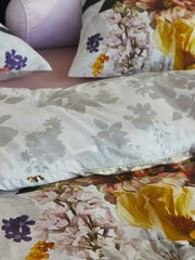 Nahaufnahme von Bettwäsche mit floralem Muster in verschiedenen Farben, darunter Gelb, Lila und Rosa, auf einem Bett.