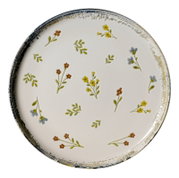 Runder cremeweißer Keramikteller mit zartem Streublumenmuster in Gelb, Blau und Braun sowie rustikalem blau-goldenem Rand, aus der Draufsicht