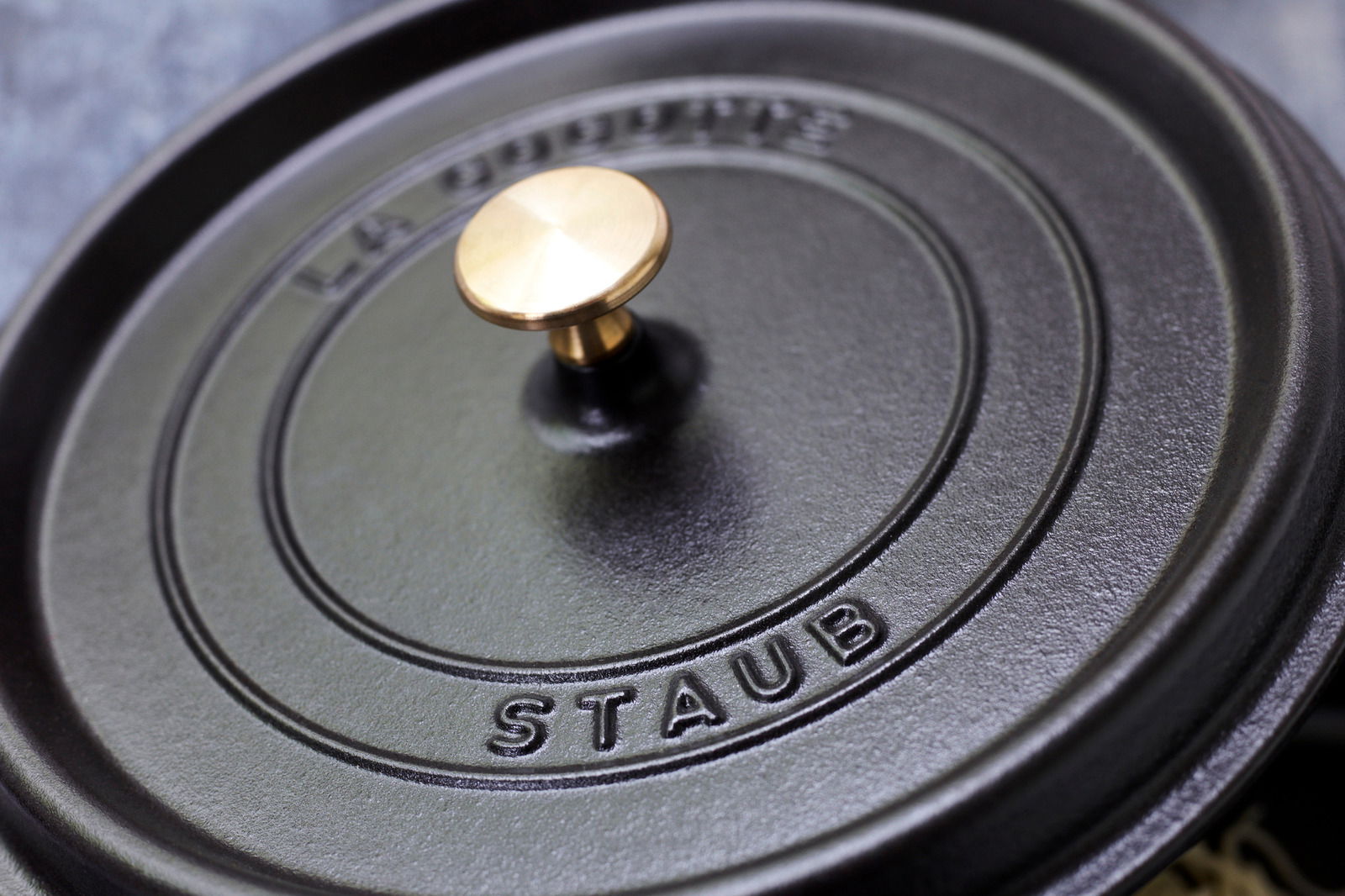 Nahaufnahme des Deckels eines runden Bräters Cocotte von Staub mit goldfarbenem Knauf, von oben betrachtet.