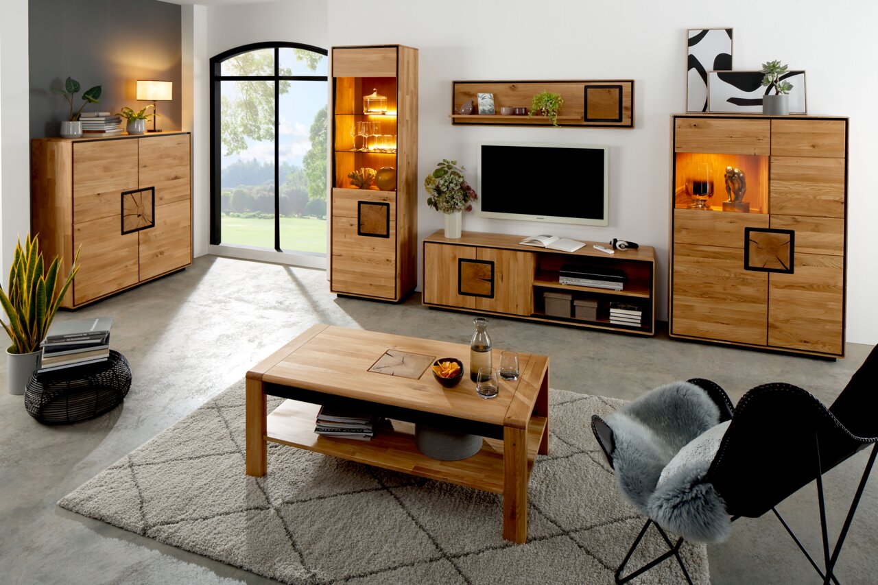 Landscape Couchtisch I BRIXEN Modernes Wohnzimmer mit Wohnwand und Couchtisch aus hellem Massivholz, Vitrinenschrank und Sideboards mit warm beleuchteten Glasfächern, TV-Board und Wandregal; Perspektive: frontale Weitwinkelaufnahme auf Augenhöhe.