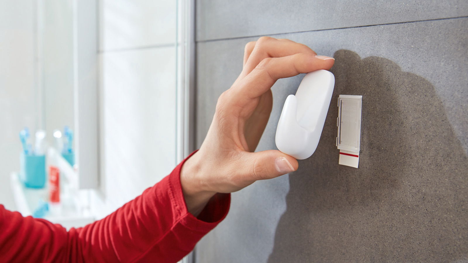 Hand befestigt einen weißen, wasserdichten tesa Powerstrip Haken an einer Badezimmerwand, seitliche Perspektive.