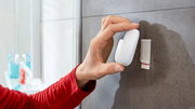 Hand befestigt einen weißen, wasserdichten tesa Powerstrip Haken an einer Badezimmerwand, seitliche Perspektive.