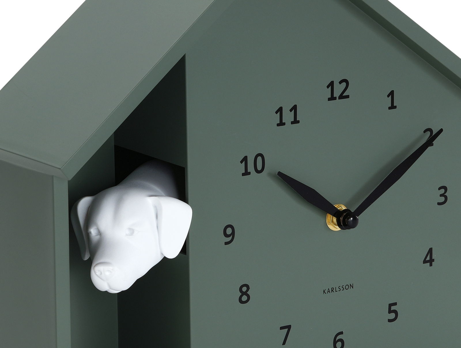 Grüne Wanduhr in Form eines Hauses mit einem weißen Hundekopf, der aus einer Öffnung herausschaut. Die Uhr hat schwarze Zeiger und Zahlen. Perspektive von schräg vorne.