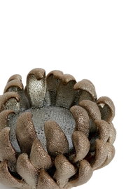 Close-up van een kunstzinnig vormgegeven theelichthouder in de vorm van een bloem, met een metalen afwerking en een gestructureerd oppervlak, gezien van bovenaf.
