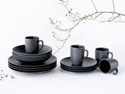 Schwarzes, matt strukturiertes Geschirr- und Tassen-Set aus Keramik mit gestapelten Tellern/Schalen und mehreren Bechern auf weißem Hintergrund, frontal aus leicht erhöhter Perspektive
