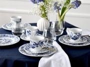Schick gedeckter Tisch mit blau-weißem Porzellanservice (Tassen und Teller), Wassergläsern, goldfarbenem Löffel und Blumenvasen auf dunkelblauer Tischdecke, perspektivisch aus leicht erhöhter, schräger Vorderansicht aufgenommen