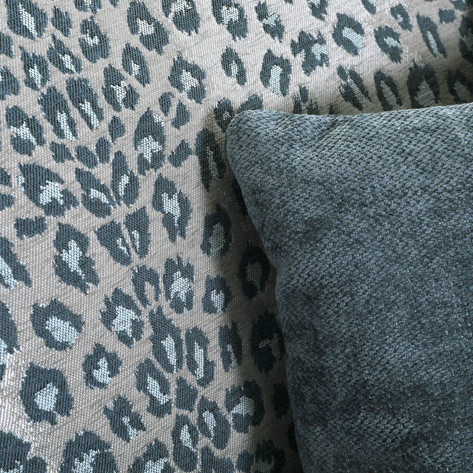 Nahaufnahme eines Sessels mit Leopardenmuster und einem dunkelgrünen Kissen, seitliche Perspektive.