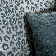 Nahaufnahme eines Sessels mit Leopardenmuster und einem dunkelgrünen Kissen, seitliche Perspektive.