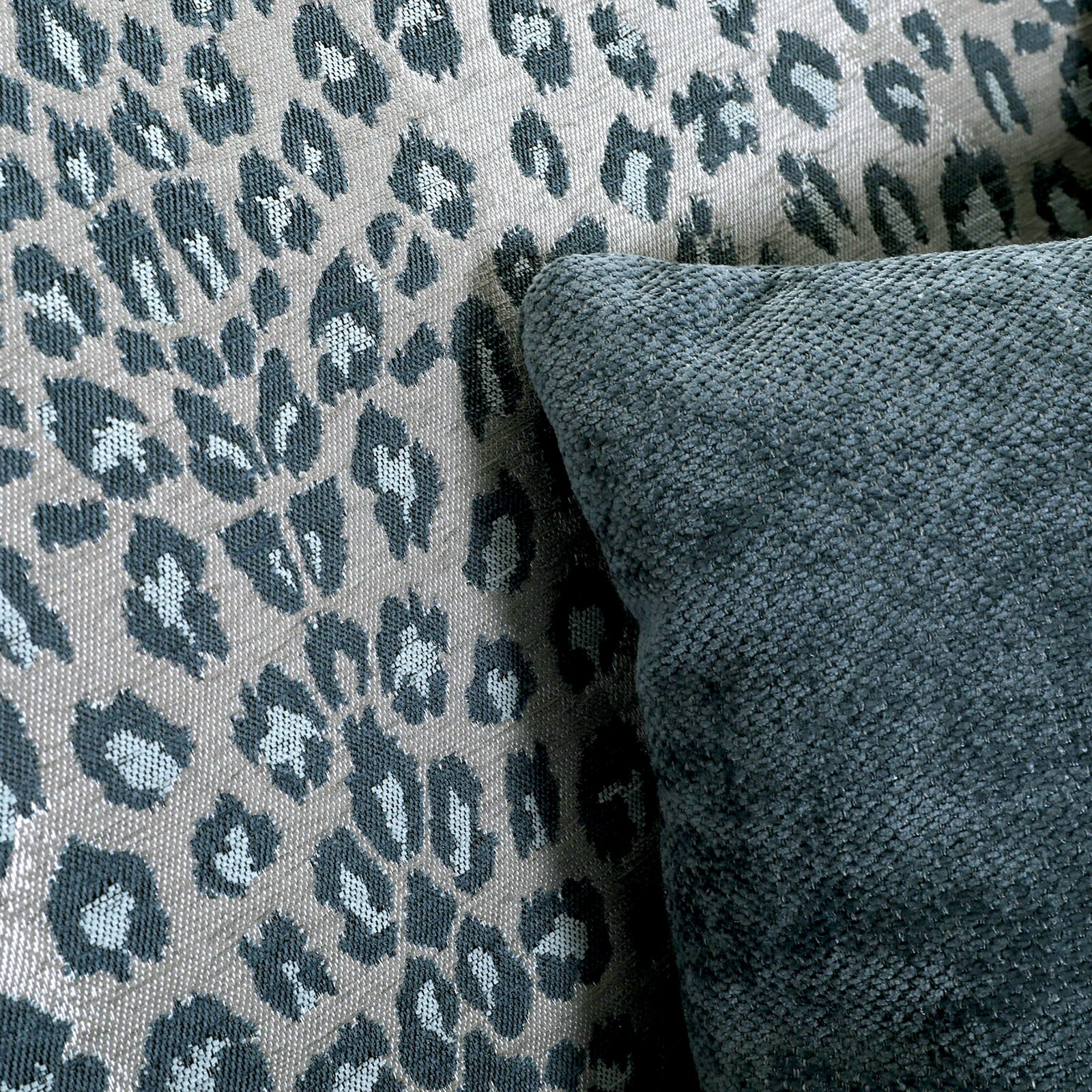 Nahaufnahme eines Sessels mit Leopardenmuster und einem dunkelgrünen Kissen, seitliche Perspektive.