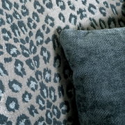 Nahaufnahme eines Sessels mit Leopardenmuster und einem dunkelgrünen Kissen, seitliche Perspektive.