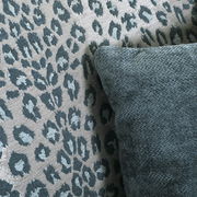 Nahaufnahme eines Sessels mit Leopardenmuster und einem dunkelgrünen Kissen, seitliche Perspektive.