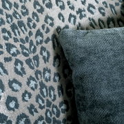 Nahaufnahme eines Sessels mit Leopardenmuster und einem dunkelgrünen Kissen, seitliche Perspektive.