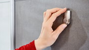 Hand befestigt einen Edelstahlhaken an einer grauen Wand aus der Seitenperspektive.