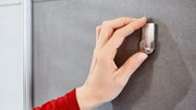 Hand befestigt einen Edelstahlhaken an einer grauen Wand aus der Seitenperspektive.