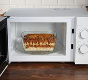 Mikrowelle mit geöffneter Tür, darin eine Glasauflaufform mit Nudelauflauf, Frontansicht