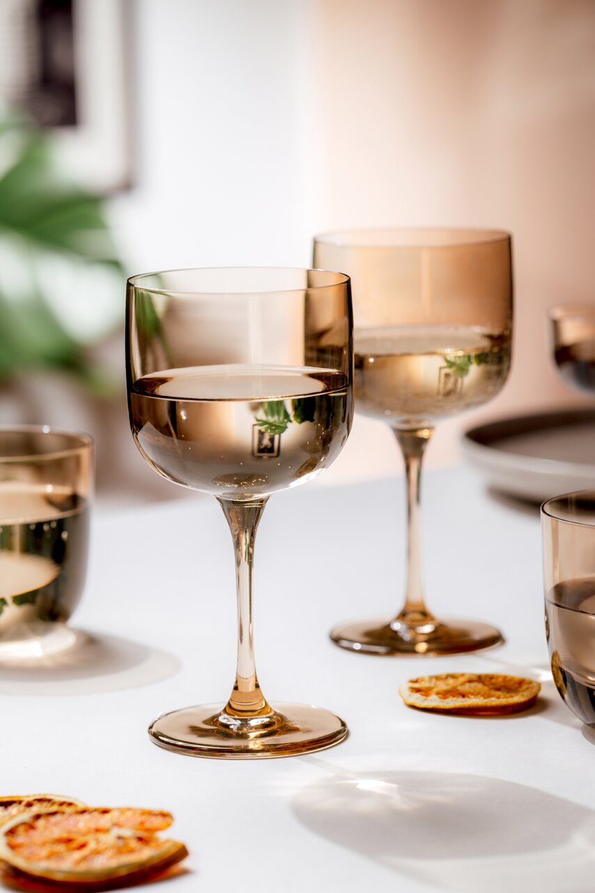 Zwei elegante Weinkelche aus Glas in warmem Licht, auf einem Tisch mit getrockneten Orangenscheiben, aus einer seitlichen Perspektive fotografiert.