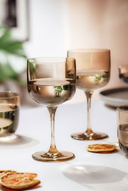 Zwei elegante Weinkelche aus Glas in warmem Licht, auf einem Tisch mit getrockneten Orangenscheiben, aus einer seitlichen Perspektive fotografiert.