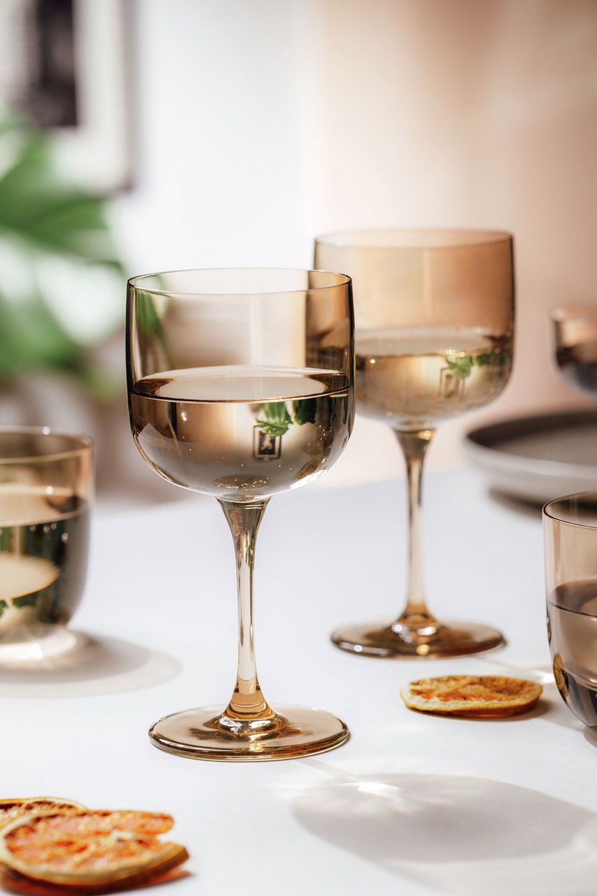 Zwei elegante Weinkelche aus Glas in warmem Licht, auf einem Tisch mit getrockneten Orangenscheiben, aus einer seitlichen Perspektive fotografiert.