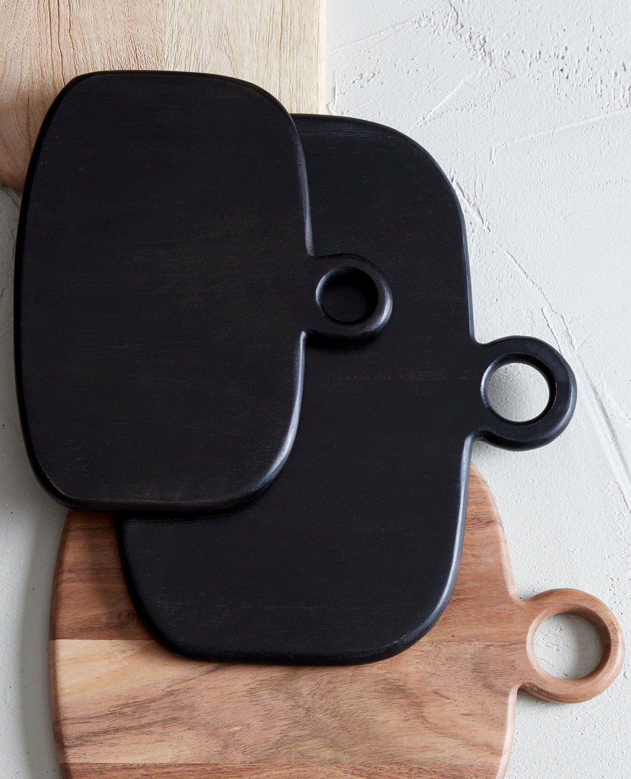 Drei übereinander gestapelte Schneidebretter aus Holz, zwei in dunklem Holzton und eines in hellem Holzton, mit runden Griffen, aus der Vogelperspektive fotografiert.