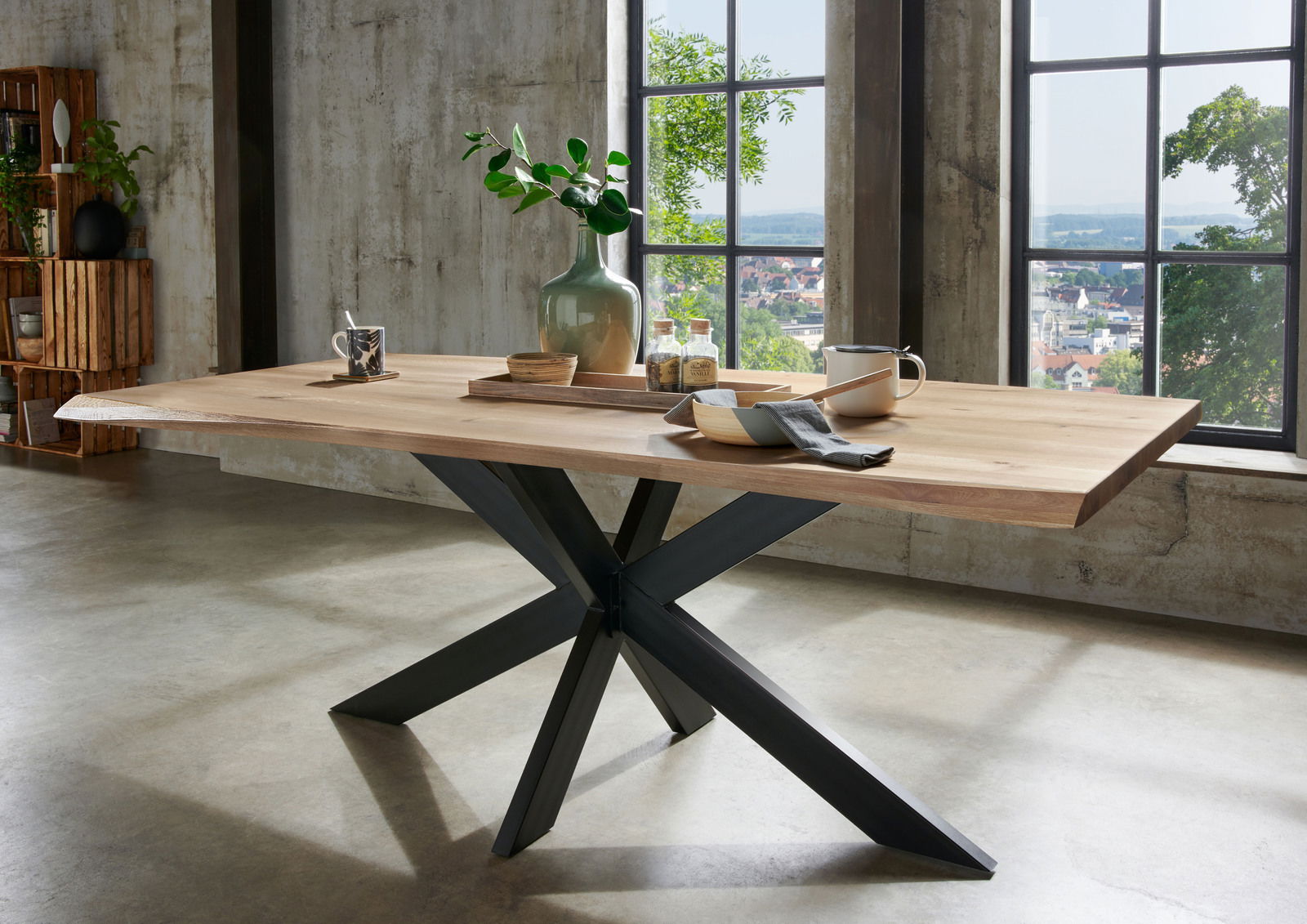 Moderner Esstisch aus Holz mit schwarzem Metallgestell, seitliche Perspektive, dekoriert mit Geschirr und Pflanzen, vor einem großen Fenster mit Blick auf die Stadt.