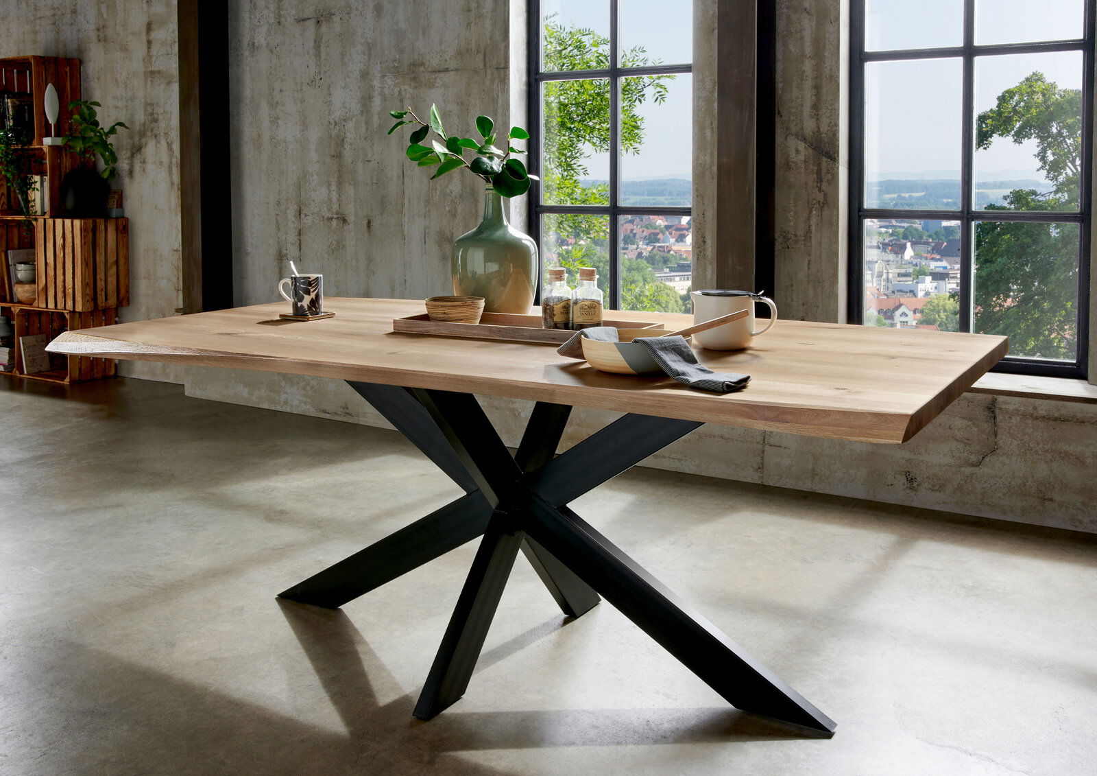 Moderner Esstisch aus Holz mit schwarzem Metallgestell, seitliche Perspektive, dekoriert mit Geschirr und Pflanzen, vor einem großen Fenster mit Blick auf die Stadt.