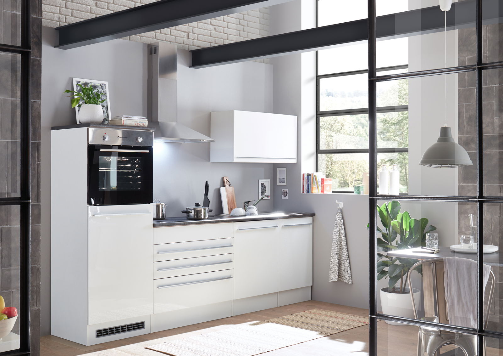 Yourkitchen Küchenblock 260 JAZZ Moderne Küche mit weißem Küchenblock, bestehend aus einem Herd, Schränken und einer Dunstabzugshaube, in einem hellen Raum mit großen Fenstern und Pflanzen. Perspektive von vorne links.