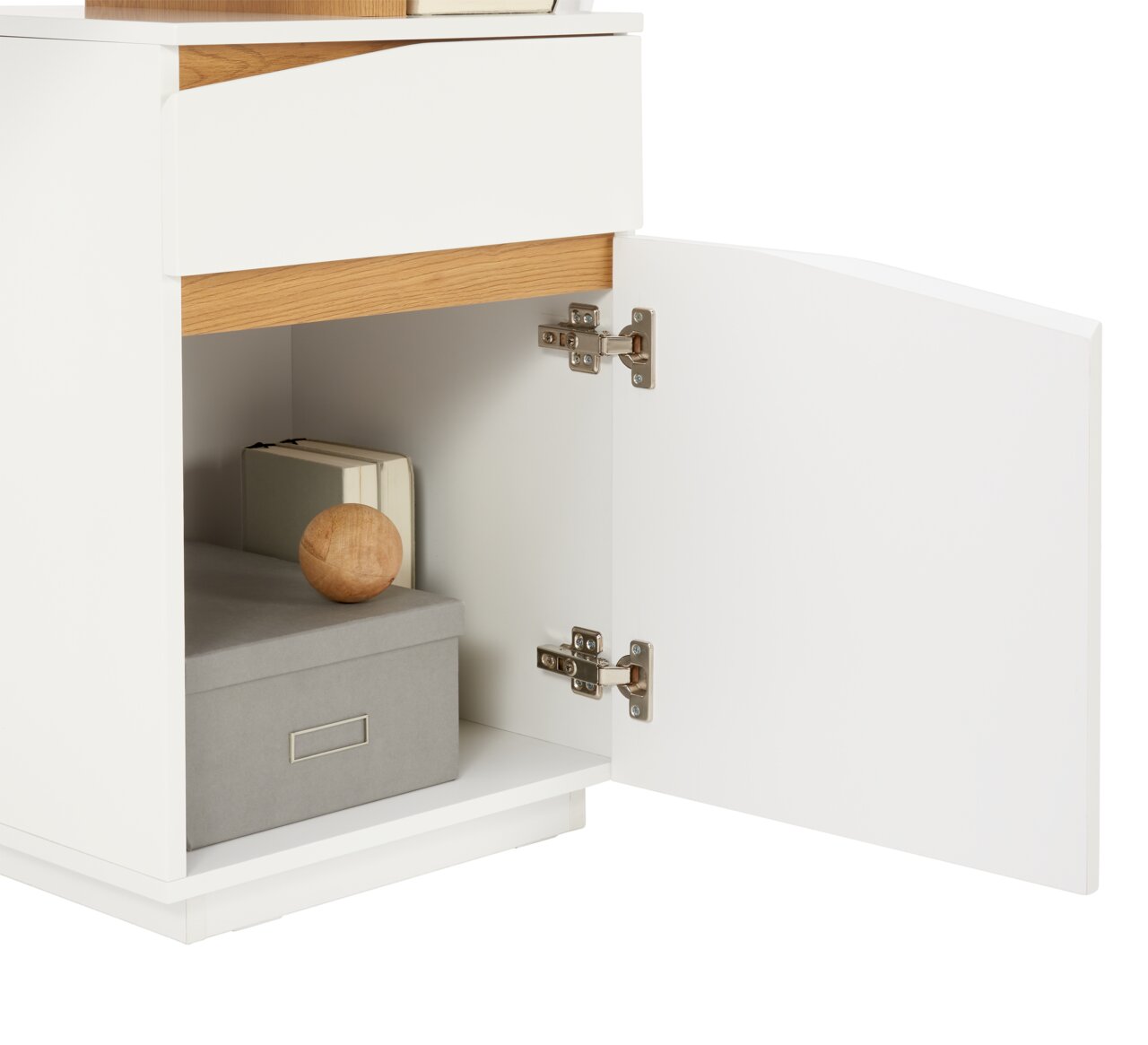 Nahaufnahme eines weißen Schreibtischs mit geöffneter Tür, die einen Stauraum mit einem Buch, einer grauen Box und einem Holzkugel zeigt. Perspektive von der Seite.