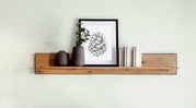 Houten wandplank met decoratie, waaronder twee vazen, een ingelijste foto en boeken, gezien vanuit het vooraanzicht.