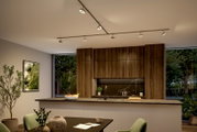 Moderne Küche mit Decken-Stromschiene und mehreren schwenkbaren Spotlights, Holzfronten und Kücheninsel mit dunkler Arbeitsplatte, aufgenommen aus leicht erhöhter Perspektive schräg von vorne