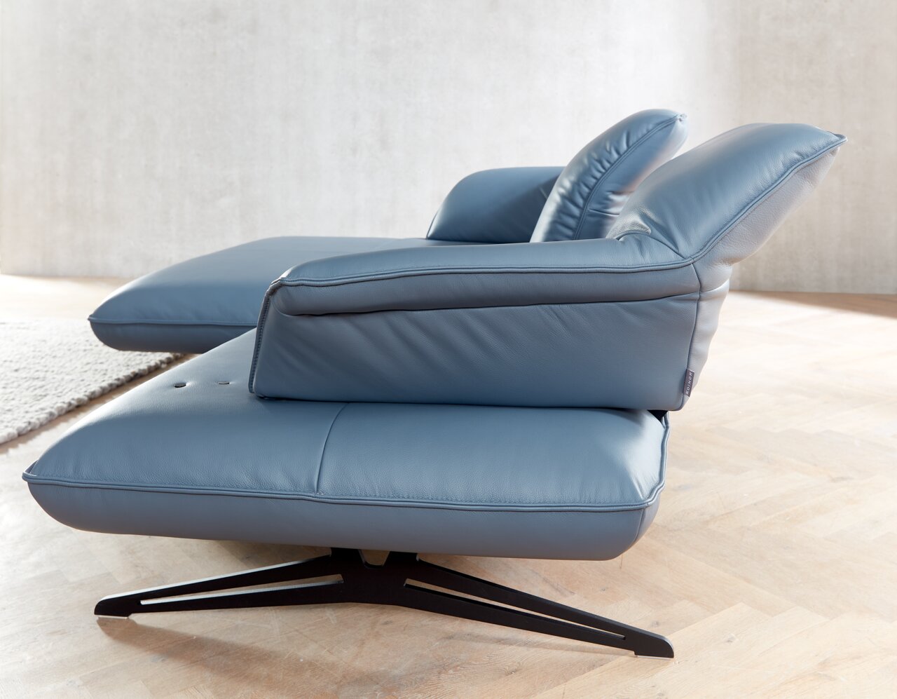 Zijaanzicht van een blauwe Koinor SEVENTY-ligstoelcombinatie met een modern ontwerp en metalen poten op een houten vloer.
