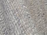 Nahaufnahme eines handgewebten Teppichs mit grauen und beigen Tönen, die Textur und Webmuster aus der Seitenperspektive zeigend.