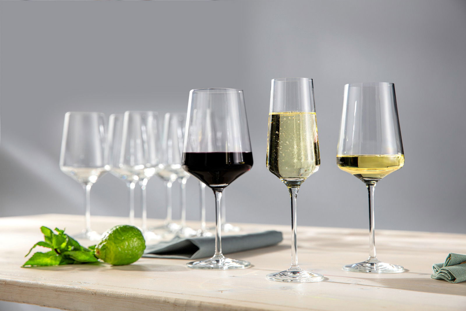 Verschiedene Weingläser auf einem Tisch, gefüllt mit Rotwein, Weißwein und Sekt, aus seitlicher Perspektive fotografiert.