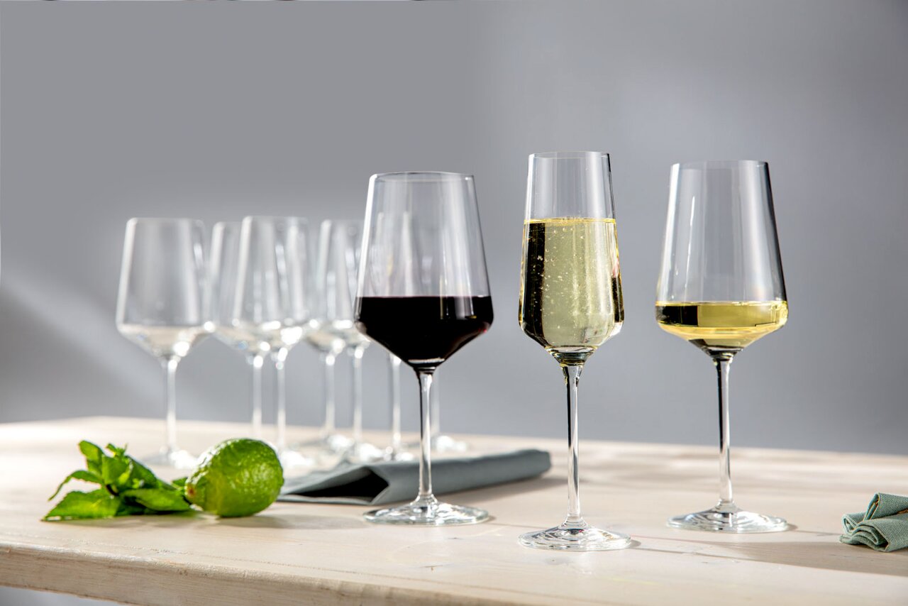 Verschiedene Weingläser auf einem Tisch, gefüllt mit Rotwein, Weißwein und Sekt, aus seitlicher Perspektive fotografiert.