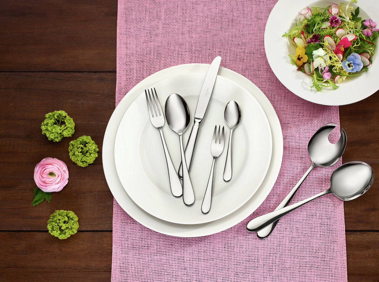 Villeroy & Boch Tafelbesteck 68-tlg.OSCAR Elegantes Tafelbesteck-Set Oscar, 68-teilig, auf einem gedeckten Tisch mit rosa Tischläufer und dekorativen Blumen, aus der Vogelperspektive fotografiert.
