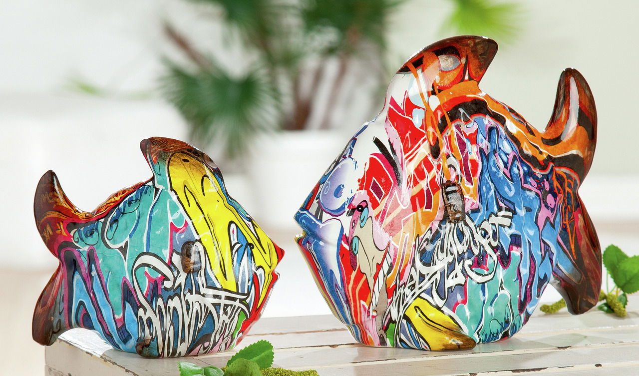Zwei bunte Fischskulpturen mit Street-Art-Motiven, die auf einem Tisch stehen. Die Perspektive zeigt die Fische von der Seite, um die lebendigen Farben und Muster hervorzuheben.