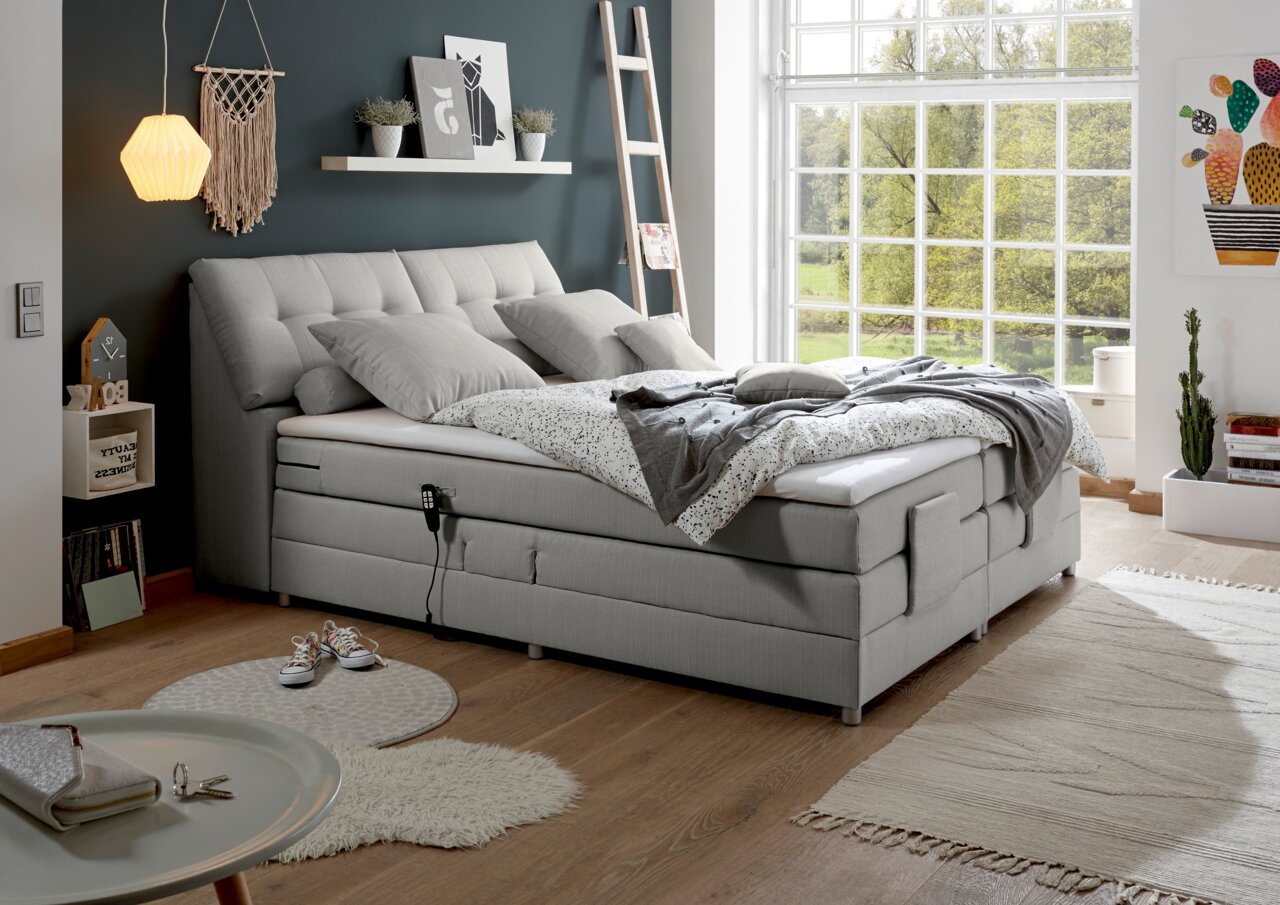 Modernes Boxspringbett in einem hellen Schlafzimmer mit großen Fenstern, seitliche Perspektive