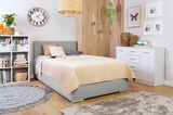 Gemütliches Boxbett 120 in einem modernen Schlafzimmer, seitliche Perspektive, mit grauem Kopfteil und beiger Steppdecke, umgeben von stilvoller Dekoration.