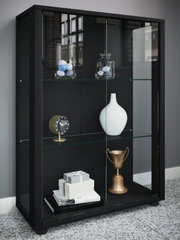 Schwarze Vitrine mit Glasböden und Schiebetüren, dekoriert mit Vasen, Uhr, Geschenkboxen und Pokal; Perspektive: frontale Ansicht leicht von links.