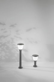 Zwei moderne Pollerleuchten in unterschiedlicher Höhe, frontal fotografiert, mit weichem Licht und Schatteneffekten an der Wand.