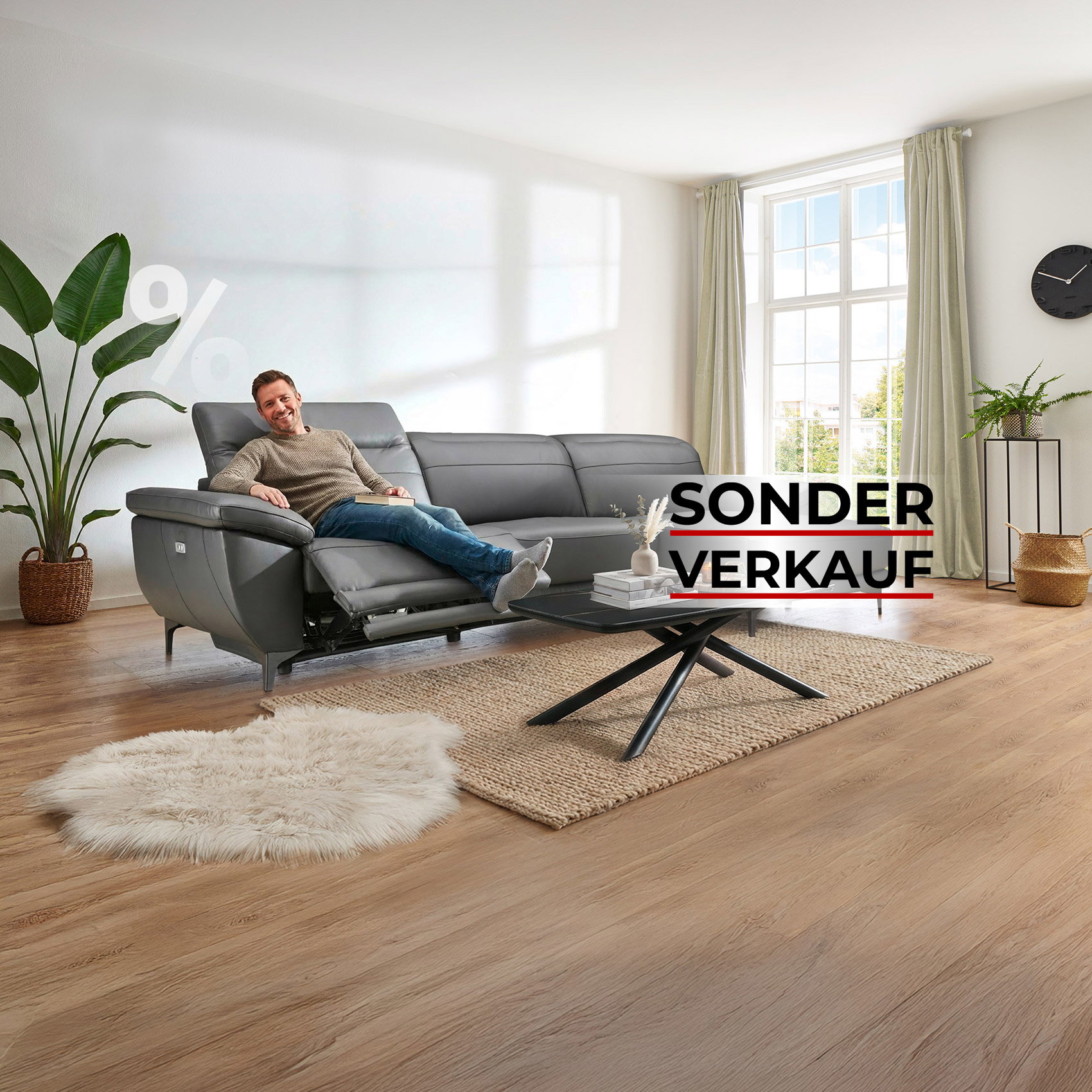 Mann entspannt auf grauem Ledersofa mit Relaxfunktion in hellem Wohnzimmer, Hinweis auf Sonderverkauf.