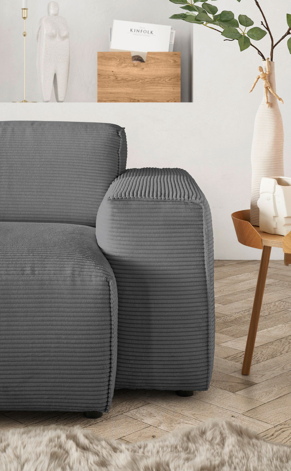 Graue Rundecke mit geripptem Stoffbezug, seitliche Perspektive, neben einem Holztisch mit Dekoration.