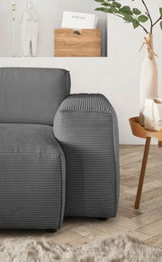 Graue Rundecke mit geripptem Stoffbezug, seitliche Perspektive, neben einem Holztisch mit Dekoration.