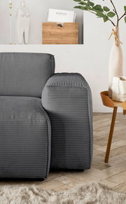 Graue Rundecke mit geripptem Stoffbezug, seitliche Perspektive, neben einem Holztisch mit Dekoration.