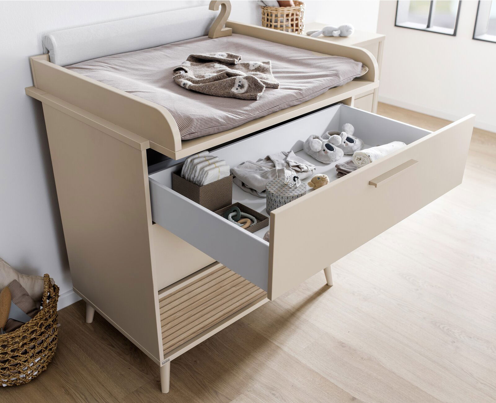 Kommode mit Wickelauflage und geöffneter Schublade, gefüllt mit Babyartikeln, aus seitlicher Perspektive fotografiert.