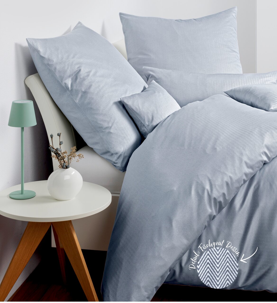 Janine Bettwäsche JERSEY-CLASSIC Bettwäsche-Set in hellgrau mit Fischgrätmuster, auf einem Bett arrangiert, mit einem Nachttisch und einer Lampe im Hintergrund, seitliche Perspektive