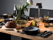 Elegantes Tafelservice 12-tlg auf einem gedeckten Tisch mit modernen Gläsern, Besteck und einer Vase mit Blumen, seitliche Perspektive.