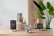 Mehrere moderne Windlichter aus Metall mit geometrischem Muster auf einem Holztisch, seitliche Perspektive.