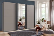 Moderner dreitüriger Schwebetürenschrank BERN in einem stilvollen Raum mit Pflanzen und einem Sessel, seitliche Perspektive.