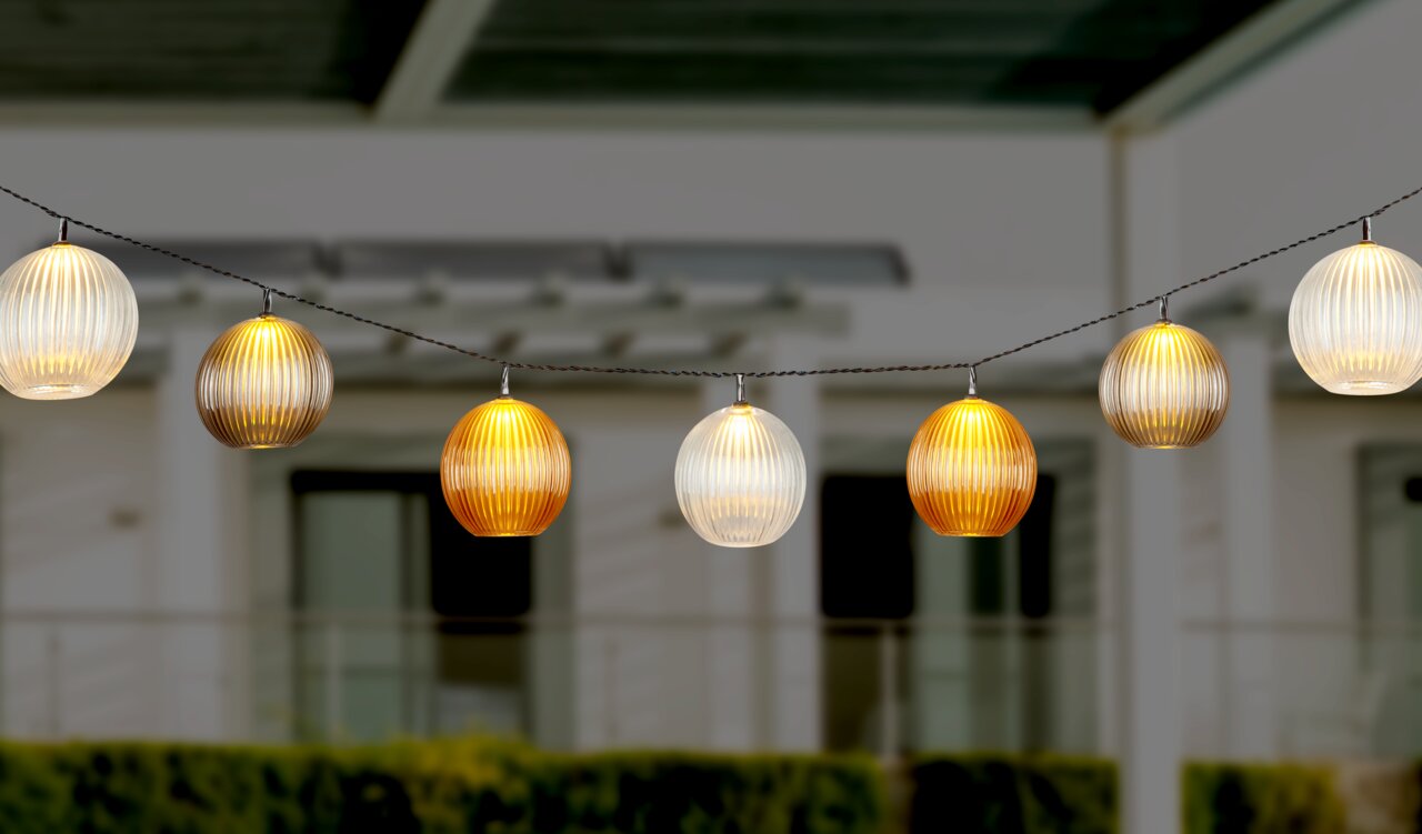 Ambia Garden Lichterkette FUNNY Lichterkette mit kugelförmigen, geriffelten Lampenschirmen in warmen Farben, aufgehängt in einem Außenbereich, seitliche Perspektive